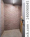 Empty storage room with exposed brick walls and concrete floor. A door is partially open, revealing a simple, minimalistic space 140090045