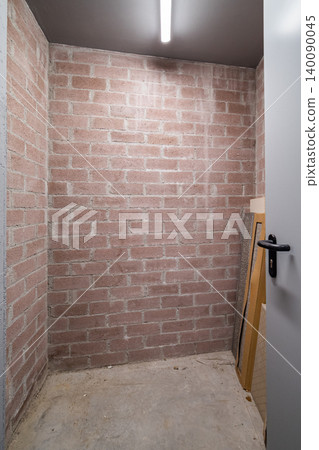 Empty storage room with exposed brick walls and concrete floor. A door is partially open, revealing a simple, minimalistic space Empty storage room with exposed brick walls and concrete floor. A door is partially open, revealing a simple, minimalistic space 140090045