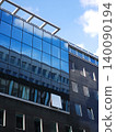 Modern glass office building reflects sky and clouds on its facade with rows of windows 140090194