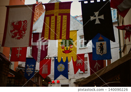 Collection of vibrant medieval heraldic banners and flags suspended across a narrow historical Collection of vibrant medieval heraldic banners and flags suspended across a narrow historical 140090226