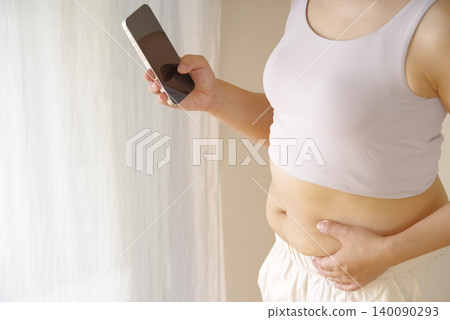 一位女士拿著智慧型手機,擔心自己的腰圍。 一位女士拿著智慧型手機,擔心自己的腰圍。 140090293