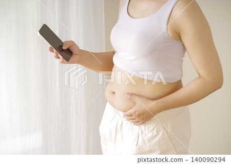 A woman holding her smartphone, concerned about her waistline. 140090294