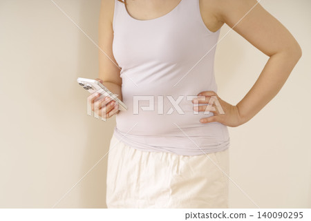 A woman holding her smartphone, concerned about her waistline. 140090295