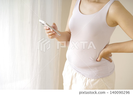 A woman holding her smartphone, concerned about her waistline. 140090296