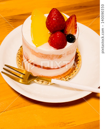 A mini cake with strawberries and peaches on a white plate, and a gold fork. A mini cake with strawberries and peaches on a white plate, and a gold fork. 140090350