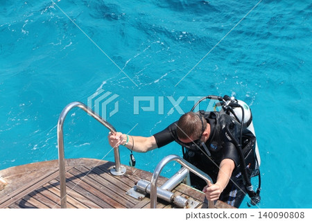 Scuba Diver Climbing Out of Blue Ocean Water onto a Boat Scuba Diver Climbing Out of Blue Ocean Water onto a Boat 140090808