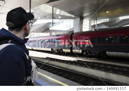 Traveler with a backpack waiting for a train on a platform at a modern railway station, illustrating train travel theme. 140091157