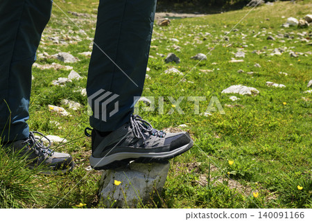 Person wearing hiking boots stepping on a rock in a grassy field in the Austrian Alps, highlighting mountain tourism. Person wearing hiking boots stepping on a rock in a grassy field in the Austrian Alps, highlighting mountain tourism. 140091166