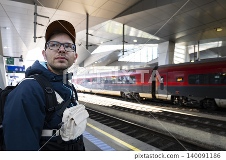 Young man with a backpack waiting for train on a platform at a modern railway station, illustrating boarding preparation. Young man with a backpack waiting for train on a platform at a modern railway station, illustrating boarding preparation. 140091186