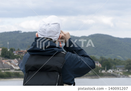 Tourist looking through a small telescope at a river landscape, emphasizing sightseeing and scenic viewpoints. 140091207