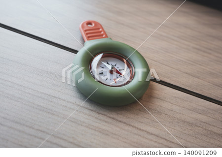 Portable green and orange compass on a wooden table, suitable for travel use and practical field tasks. Portable green and orange compass on a wooden table, suitable for travel use and practical field tasks. 140091209