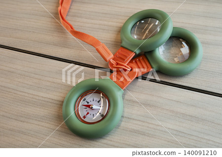 Outdoor adventure kit with a compass and magnifying glasses on a wooden table, presenting a compact outdoor exploration tool. 140091210