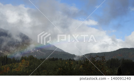 Rainbow arc over a foggy mountain landscape with clouds in the Austrian Alps, highlighting a striking natural weather phenomenon. 140091240