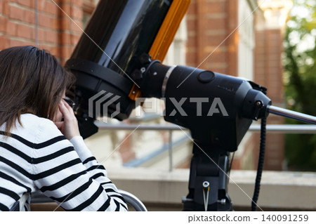 Person observing the sky through a telescope during a science lab open house, highlighting public engagement with astronomy. Person observing the sky through a telescope during a science lab open house, highlighting public engagement with astronomy. 140091259