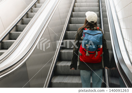 Young woman with a backpack on an escalator at a railway station, highlighting modern travel and transit infrastructure. Young woman with a backpack on an escalator at a railway station, highlighting modern travel and transit infrastructure. 140091263
