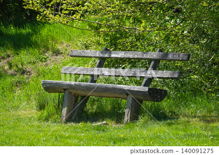 Rustic bench on fresh green grass in the forest offering a relaxation in a peaceful atmosphere. Rustic bench on fresh green grass in the forest offering a relaxation in a peaceful atmosphere. 140091275