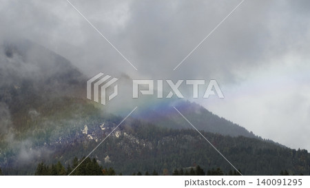 Rainbow arc over a foggy mountain landscape with clouds in the Austrian Alps, creating an atmospheric view with color contrast. Rainbow arc over a foggy mountain landscape with clouds in the Austrian Alps, creating an atmospheric view with color contrast. 140091295