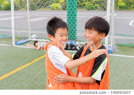Boys hug each other with smiles on their faces after scoring a goal in soccer. 140091607