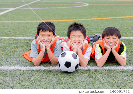 A team of boys smiles as they gather around a soccer ball. 140091731