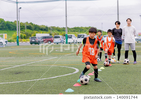 A male coach and some boys giving dribbling instruction during futsal practice. A male coach and some boys giving dribbling instruction during futsal practice. 140091744