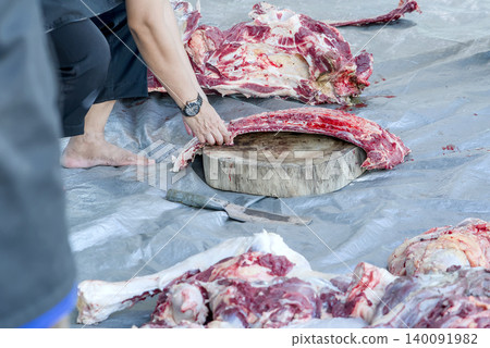 Butcher chopping raw meat with a cleaver on a wooden cutting board 140091982