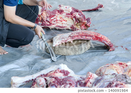 Butcher chopping raw meat with a cleaver on a wooden cutting board Butcher chopping raw meat with a cleaver on a wooden cutting board 140091984