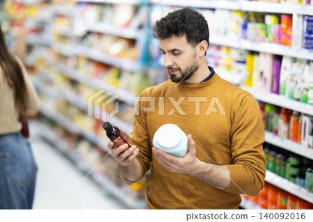 Young man choosing body and hair care products in supermarket Young man choosing body and hair care products in supermarket 140092016
