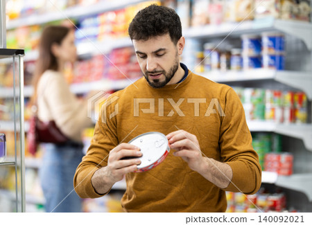 Male shopper are choosing canned fish in food store 140092021