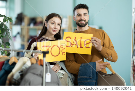 Couple holding posters with discounts and sale in the store Couple holding posters with discounts and sale in the store 140092041