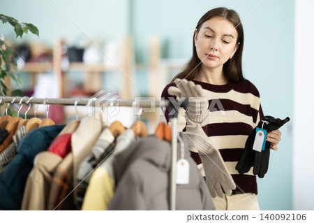 Elegance young woman choosing stylish warm gloves for cold season in clothing boutique Elegance young woman choosing stylish warm gloves for cold season in clothing boutique 140092106