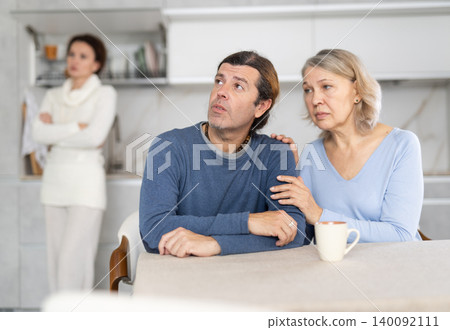 Woman scolding man at kitchen while old woman calming him down Woman scolding man at kitchen while old woman calming him down 140092111