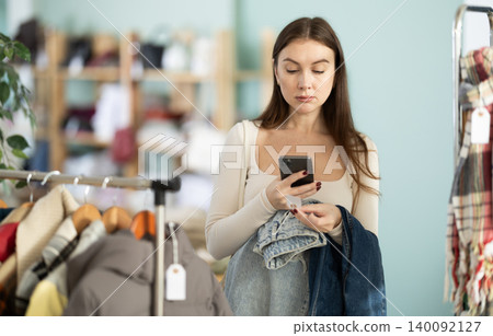 Young woman scanning QR-code on jeans pantaloons in clothing store Young woman scanning QR-code on jeans pantaloons in clothing store 140092127