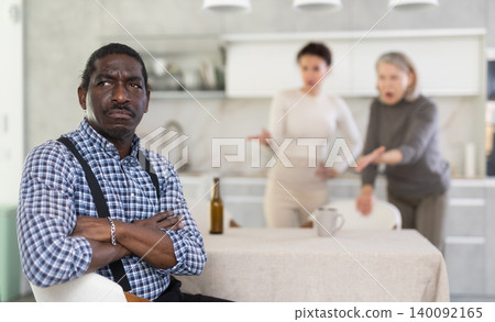 Tense man listens to two women shouting at him in kitchen 140092165