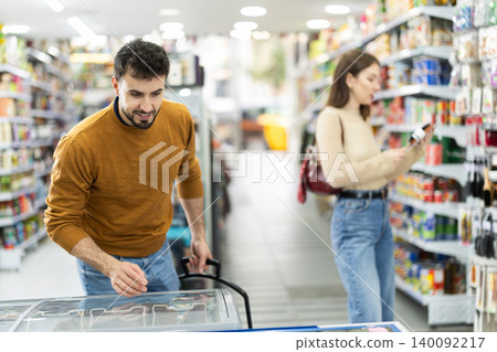 Young man choosing frozen food in grocery store Young man choosing frozen food in grocery store 140092217