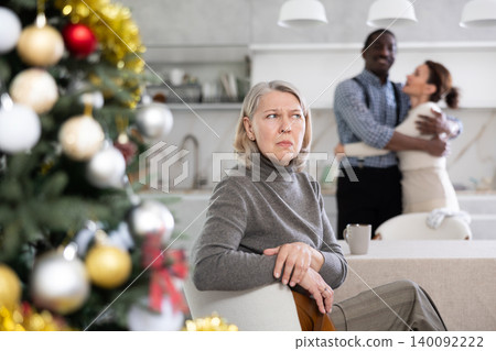 Elderly woman sad in kitchen with happy couple Elderly woman sad in kitchen with happy couple 140092222