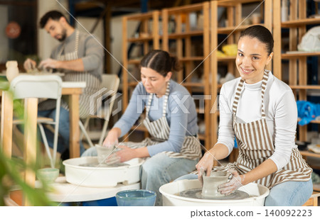 Woman in ceramics workshop with pottery wheel and various clay vessels 140092223