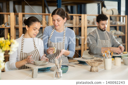 Woman help girl sculpting ceramic product from raw clay in workshop Woman help girl sculpting ceramic product from raw clay in workshop 140092243
