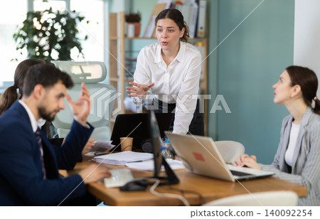 Young female manager standing and scolding colleagues during stressful corporate meeting 140092254
