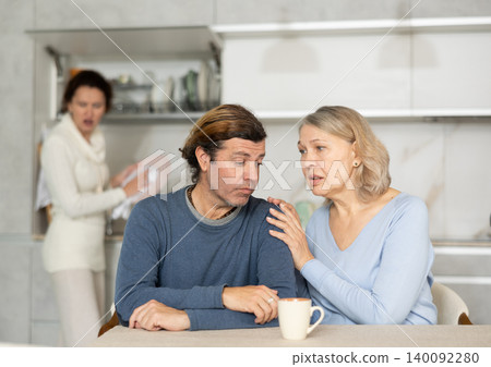 Senior woman sits near adult son and comforts him during quarrel with wife. Senior woman sits near adult son and comforts him during quarrel with wife. 140092280