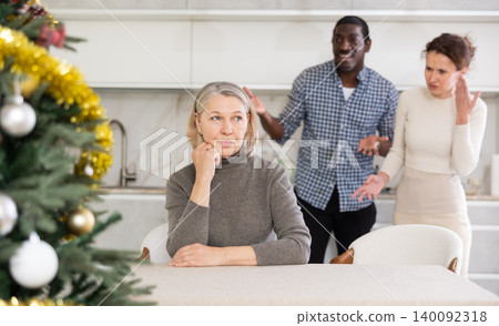 Upset old woman sitting at table with her back to angry middle-aged couple quarreling to her Upset old woman sitting at table with her back to angry middle-aged couple quarreling to her 140092318