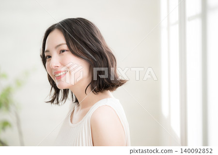 一張特寫鏡頭,一位面帶微笑的女子在自然光線充足的房間裡凝視著窗外,展現了她的美麗和自然的生活方式。 一張特寫鏡頭,一位面帶微笑的女子在自然光線充足的房間裡凝視著窗外,展現了她的美麗和自然的生活方式。 140092852