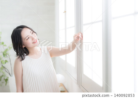 一位微笑的女子凝視著窗外,房間裡沐浴著自然光,象徵著她晨間美容的習慣和自然的生活方式。 一位微笑的女子凝視著窗外,房間裡沐浴著自然光,象徵著她晨間美容的習慣和自然的生活方式。 140092853
