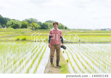 A rice farmer standing on the embankment of a rice paddy. 140093148