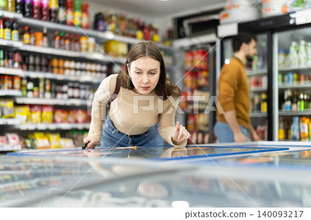 Woman spends time in store, looking for necessary goods and get out from refrigerator Woman spends time in store, looking for necessary goods and get out from refrigerator 140093217