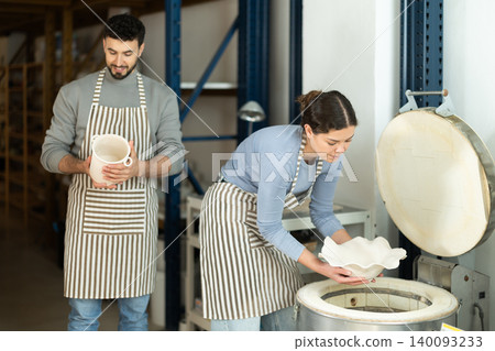 Girl in apron put or takes clay vase out of oven Girl in apron put or takes clay vase out of oven 140093233