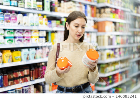 Woman spends time in store, looking for goods and select care product Woman spends time in store, looking for goods and select care product 140093241