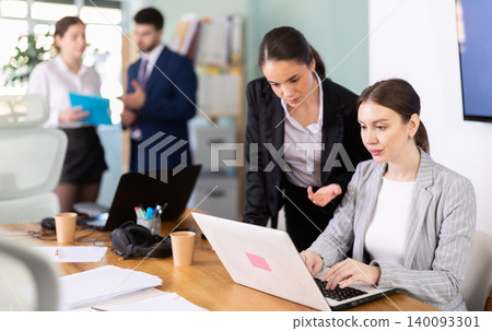 Young woman helping female colleague work on laptop Young woman helping female colleague work on laptop 140093301