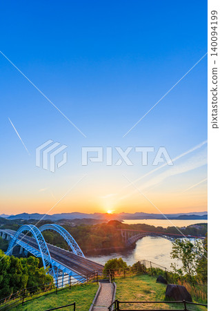 The Saikai Bridge and the sunrise as seen from the Saikai Hill Observatory in early summer, Saikai City, Nagasaki Prefecture. The Saikai Bridge and the sunrise as seen from the Saikai Hill Observatory in early summer, Saikai City, Nagasaki Prefecture. 140094199