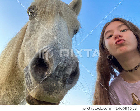 Teenager enjoying summer day in countryside, taking a selfie with a curious white horse, showing connection, friendship, and affection for animals outdoors Teenager enjoying summer day in countryside, taking a selfie with a curious white horse, showing connection, friendship, and affection for animals outdoors 140094512