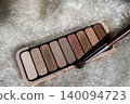 Nude eyeshadow palette with multiple shimmer and matte shades, presenting a range of warm and neutral tones for versatile everyday beauty looks, resting on a soft white background 140094723